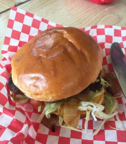 A juicy burger with lettuce, tomato, and grilled onions on a toasted bun, served on a red and white checkered paper.