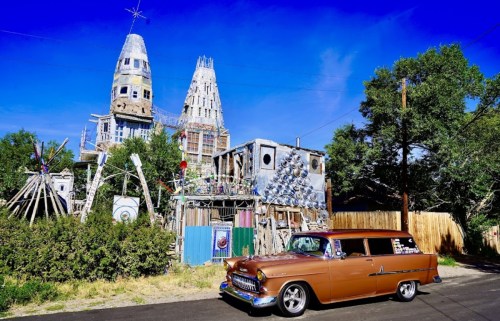 A vintage car parked in front of a whimsical, colorful house with unique architectural features and sculptures.