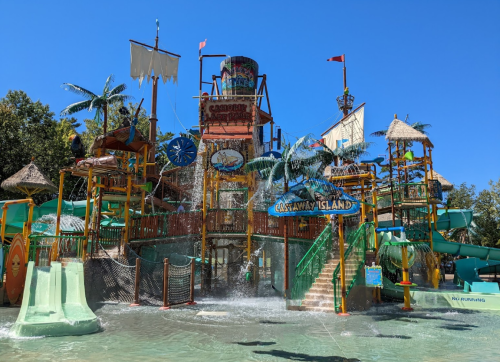 Colorful water park structure with slides, palm trees, and a large water feature under a clear blue sky.