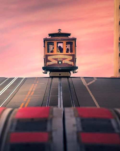 A cable car ascends a steep hill against a colorful sunset sky, showcasing urban scenery and iconic transportation.