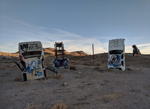 Graffiti-covered car doors stand in a barren landscape with mountains in the background under a clear sky.