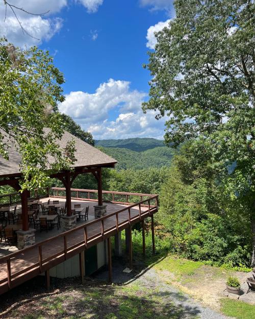 A wooden deck overlooks lush green mountains under a blue sky with fluffy clouds.
