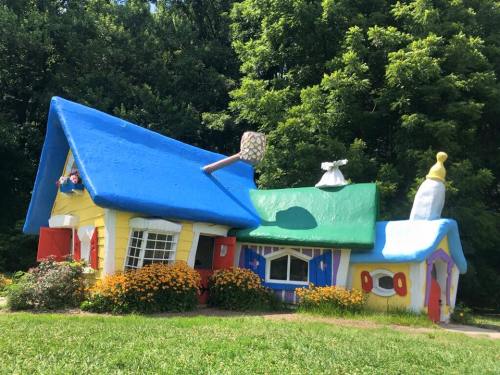 A whimsical, colorful house with a blue roof, yellow walls, and vibrant flowers in front, surrounded by greenery.