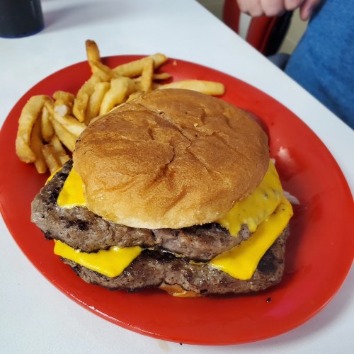A double cheeseburger with two patties and melted cheese, served with a side of curly fries on a red plate.