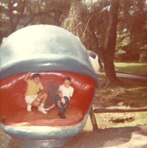 Two children sitting inside a large, colorful whale sculpture in a park, smiling and enjoying their time.