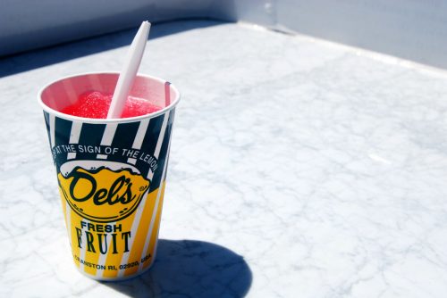 A colorful cup of frozen fruit drink with a white straw, sitting on a marble surface.