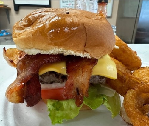 A close-up of a burger with bacon, cheese, lettuce, and tomato, served with onion rings on the side.
