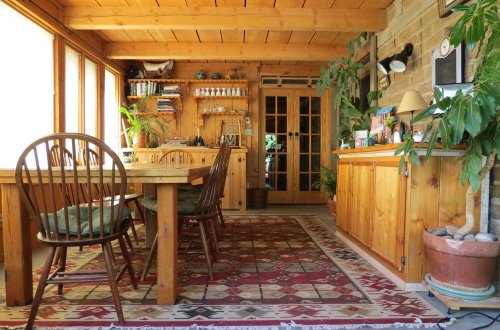 Cozy wooden dining area with a table, chairs, plants, and a sideboard, featuring a warm, rustic decor.