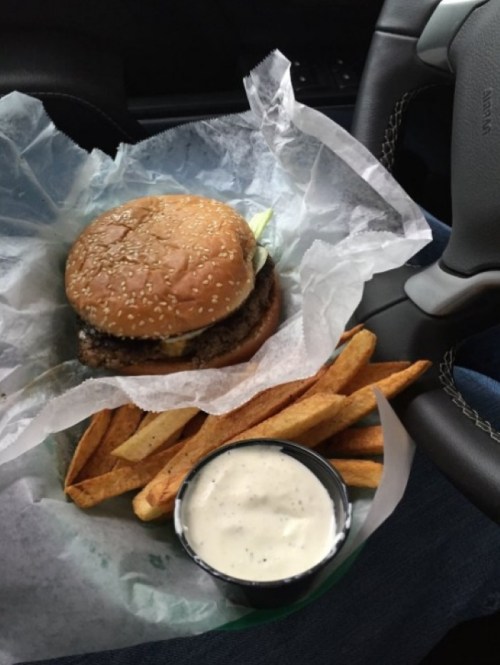 A sesame seed burger with lettuce and pickles, served with seasoned fries and a side of ranch dressing in a car.