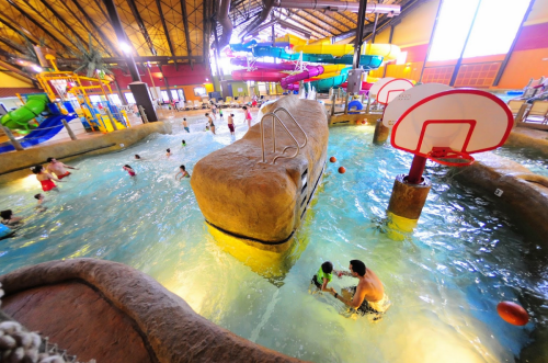 A vibrant indoor water park with slides, a rock feature, and families enjoying the pool area.