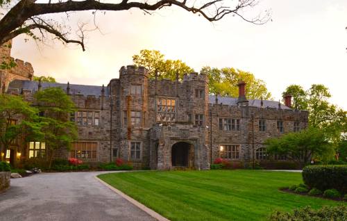 A stone castle with turrets, surrounded by green lawns and trees, under a soft sunset sky.
