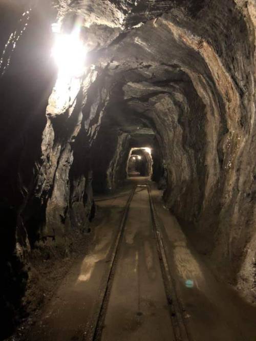 A dimly lit underground tunnel with rocky walls and railway tracks running through it.