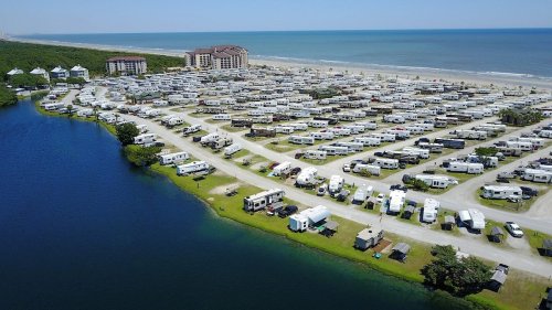 Aerial view of a large RV park by the beach, with numerous parked RVs and a lake nearby.