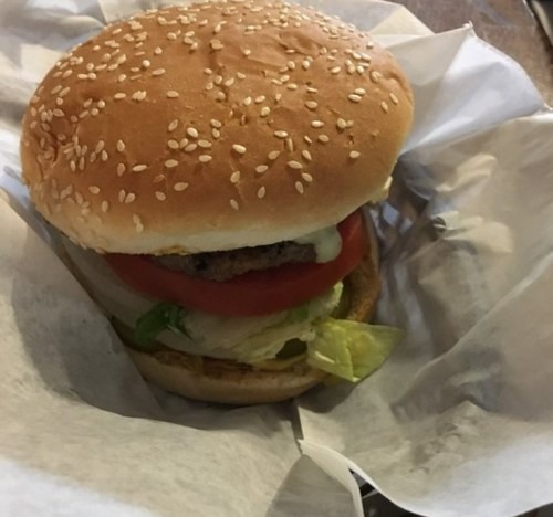 A sesame seed bun burger with lettuce, tomato, and a patty, wrapped in white paper.