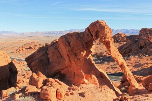 A large, unique rock formation resembling an elephant trunk in a desert landscape with distant mountains.