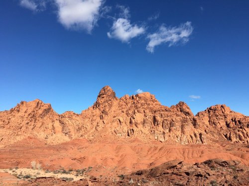 A rugged landscape of red rock formations under a clear blue sky with a few clouds.