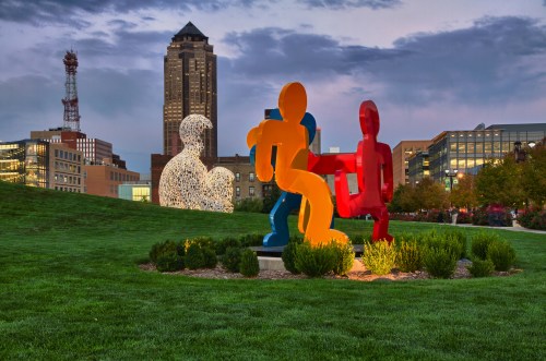 Colorful abstract sculptures in a park with a city skyline in the background during twilight.