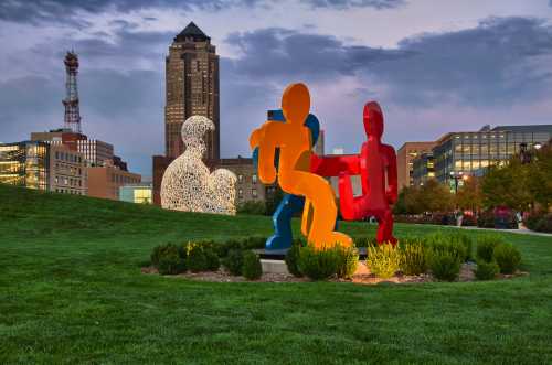 Colorful abstract sculptures in a park with a city skyline in the background during twilight.