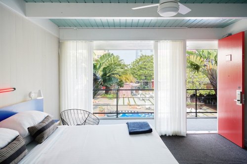 Bright hotel room with a bed, large windows, and a view of greenery and a pool area outside.