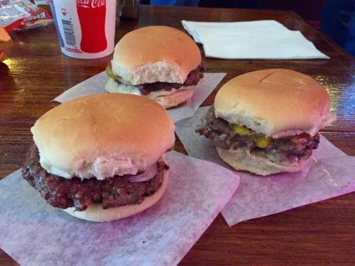 Three small burgers on paper, featuring beef patties and soft buns, placed on a wooden table.
