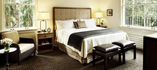 Cozy hotel room featuring a king-sized bed, armchair, and bedside tables with lamps, surrounded by natural light.