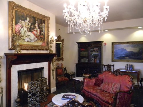 Elegant living room with a chandelier, ornate furniture, a fireplace, and classic artwork on the walls.