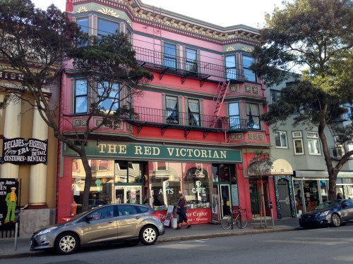 Colorful building with red exterior and decorative details, featuring "The Red Victorian" sign and a café below.