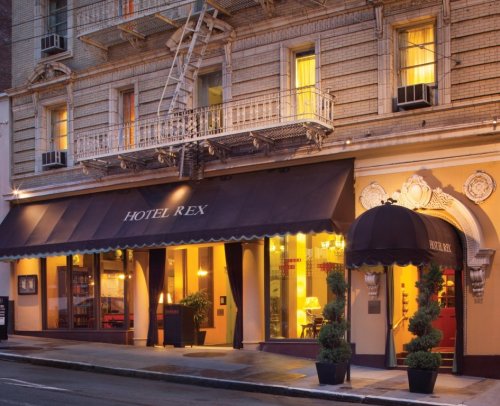 Exterior view of Hotel Rex, featuring a classic facade, awning, and decorative elements, with warm lights glowing from the windows.