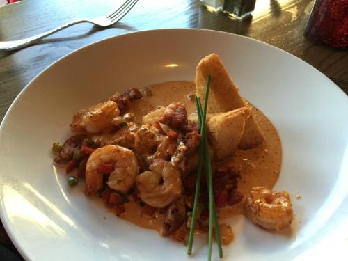 A plate of shrimp in a creamy sauce, garnished with chives and served with two triangular corn tortillas.