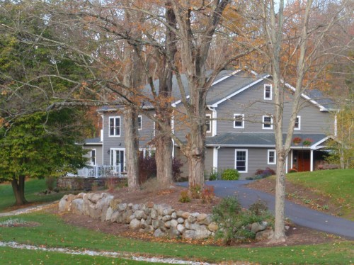 A large gray house surrounded by trees and a stone wall, set in a colorful autumn landscape.