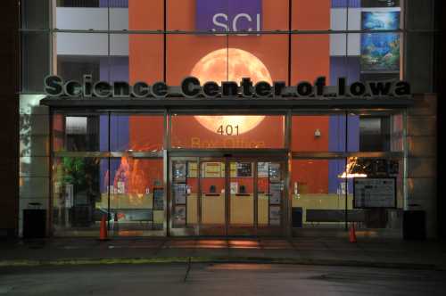 Exterior view of the Science Center of Iowa at night, featuring a large moon backdrop and illuminated entrance.