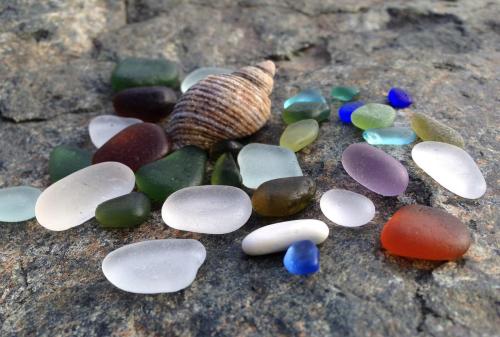 A collection of colorful sea glass pieces and a shell arranged on a rocky surface.