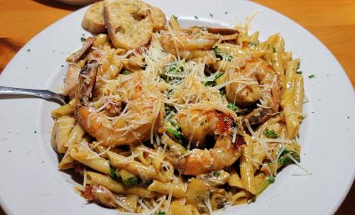 A plate of pasta with shrimp, herbs, and grated cheese, served with slices of toasted bread.