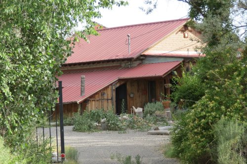 A rustic house with a red metal roof, surrounded by greenery and a gravel pathway leading to the entrance.