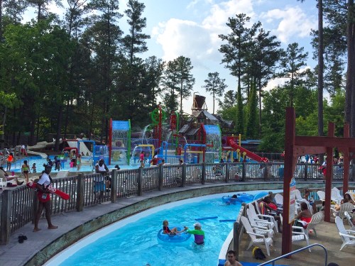 A vibrant water park scene with pools, slides, and families enjoying the attractions under a sunny sky.