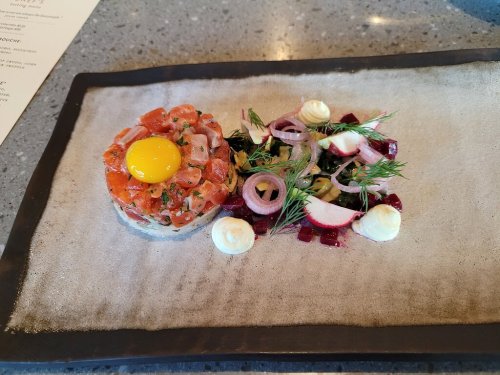A gourmet dish featuring salmon tartare topped with an egg yolk, accompanied by a colorful salad of beets and onions.