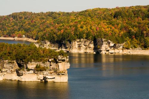 Scenic view of a lake surrounded by colorful autumn foliage and rocky cliffs under a clear sky.