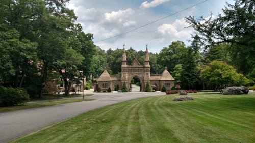 A stone archway entrance surrounded by lush greenery and trees under a partly cloudy sky.