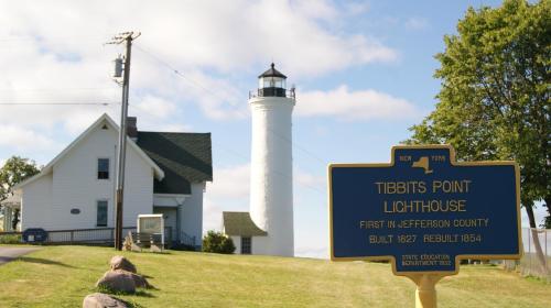 Tibbits Point Lighthouse in New York, with a white tower and adjacent historic building, surrounded by green grass.