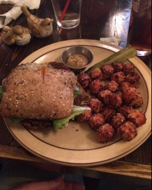 A plate with a sandwich on whole grain bread, lettuce, a pickle, and a side of crispy tater tots.
