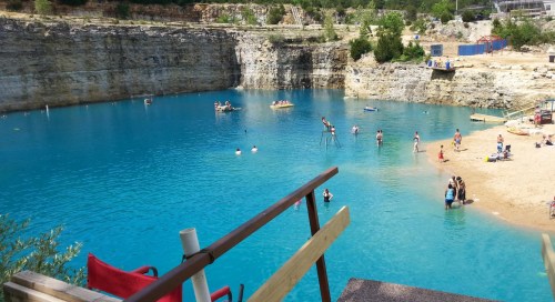 A scenic blue lake surrounded by rocky cliffs, with people swimming and relaxing on the beach.