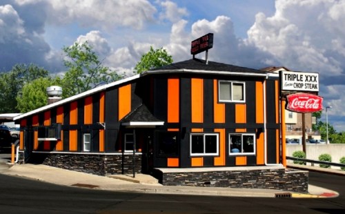 A colorful restaurant with orange and black exterior, featuring a stone base and a sign for "Triple XXX Steak."