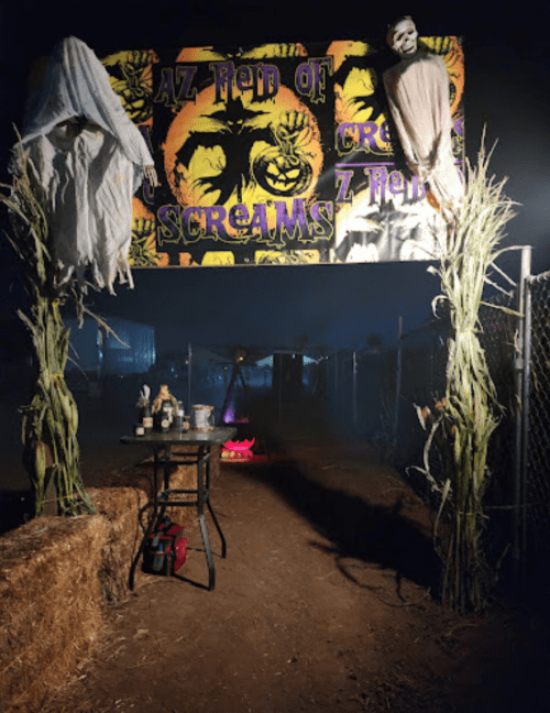 A spooky entrance to a haunted cornfield, featuring scarecrows and a sign that reads "AZ Field of Screams."