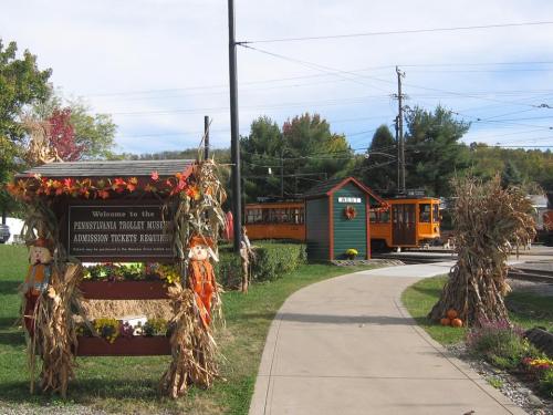A welcoming sign for the Pennsylvania Trolley Museum, with a vintage trolley and autumn decorations along a pathway.