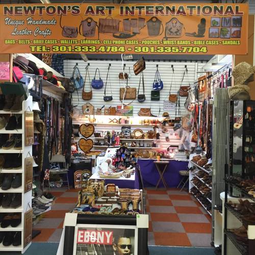A vibrant shop display featuring handmade leather bags, accessories, and crafts, with a colorful sign above.