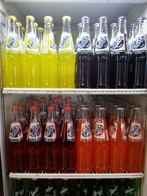 A refrigerator filled with colorful bottles of Fanta soda in various flavors, including yellow, orange, and black.