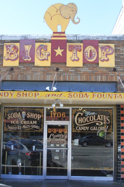 A colorful storefront of "Big Top Candy Shop" featuring an elephant sign, with ice cream and candy offerings displayed.