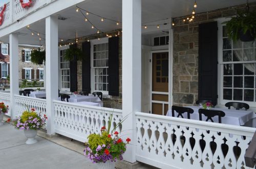 Charming restaurant exterior with white railings, tables set for dining, and hanging plants under string lights.