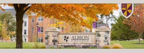Sign for Albion College surrounded by colorful autumn trees and buildings in the background.
