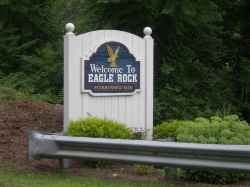 Sign welcoming visitors to Eagle Rock, established in 1879, surrounded by greenery.